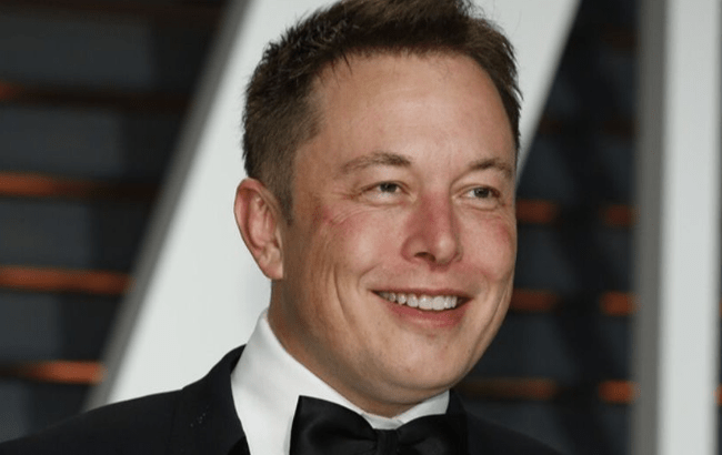 Elon Musk in a tuxedo with a black bow tie smiling at an event.