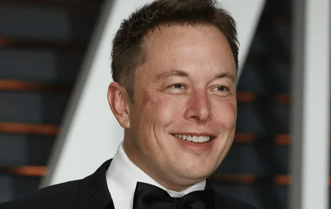 Elon Musk in a tuxedo with a black bow tie smiling at an event.